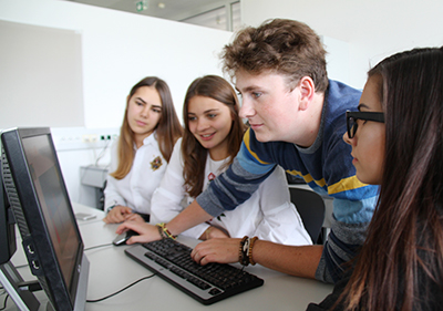 Drei Schülerinnen und ein Schüler am PC in der HAK Neusiedl am See